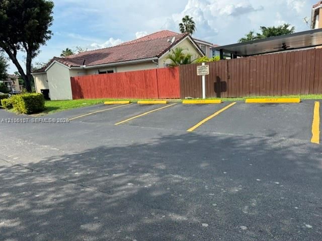 Asphalt surface parking area with four designated stalls, painted yellow wheel stops, and a tall wood perimeter fence