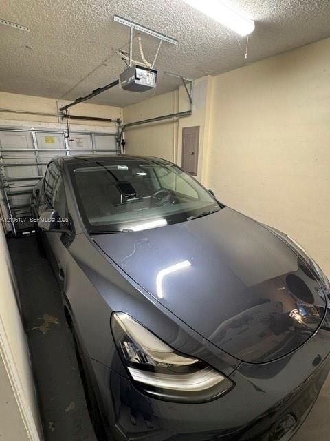 Enclosed garage featuring an automated overhead door opener, linear lighting fixture, and electrical service panel