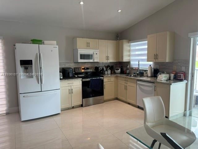 Kitchen featuring off-white shaker cabinetry, polished stone countertops, tile backsplash, stainless steel appliances, and large-format tile flooring