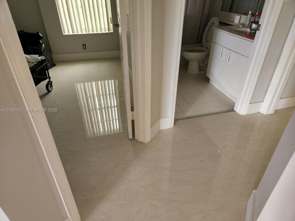 Polished large-format tile flooring, vanity with integrated basin, and window featuring vertical blinds