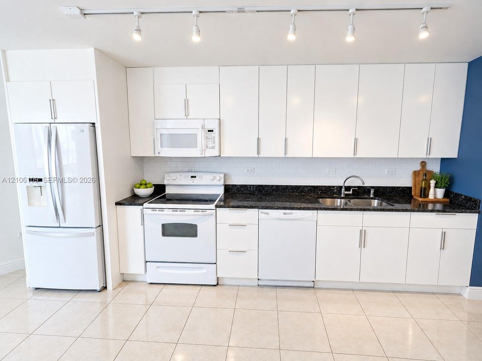Kitchen featuring white cabinetry, dark stone countertops, tile flooring, integrated white appliances, and a ceiling-mounted track lighting system