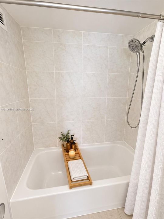 Full-size bathtub featuring floor-to-ceiling neutral tile surround and a multi-setting handheld showerhead assembly