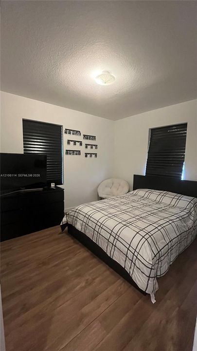 Room featuring wood-finish flooring, white walls, and two windows with black window treatments