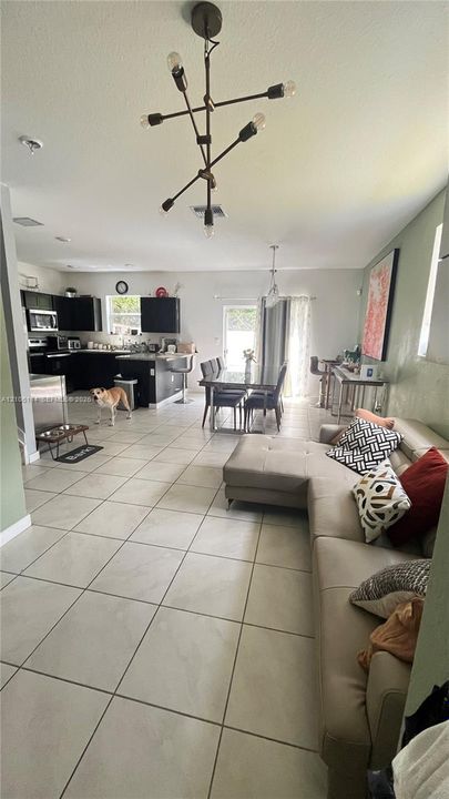 Open-concept interior featuring large-format tile flooring, modern multi-arm chandelier lighting, and a kitchen equipped with dark cabinetry