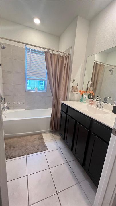 Bathroom featuring a dark wood-finish vanity with a white countertop, a white soaking tub with a tiled surround, a large wall-mounted mirror, and tile flooring