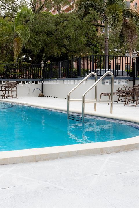 Swimming pool with light-colored concrete decking, metal handrail, perimeter black metal fencing, and decorative stone wall accents