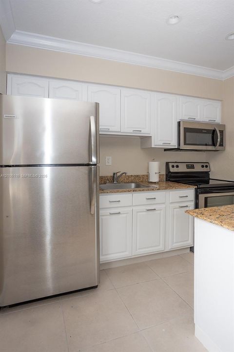 Kitchen featuring white shaker-style cabinetry, stone-finish countertops, stainless steel refrigerator, built-in stainless steel microwave, and tile flooring