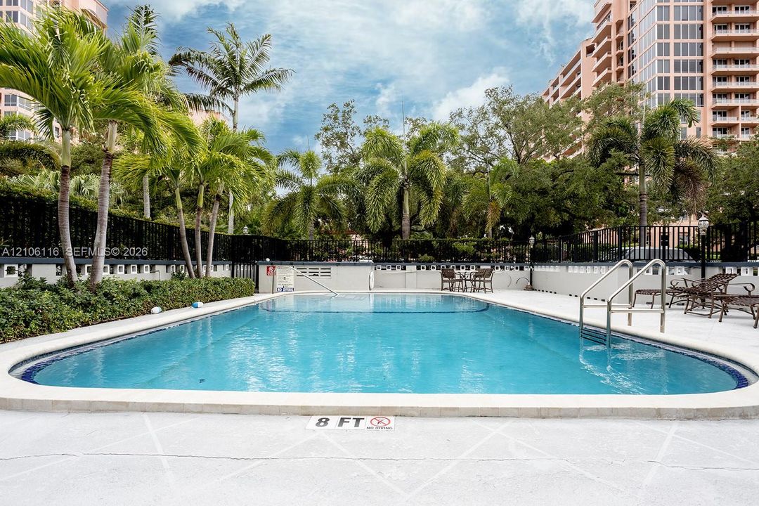 Swimming pool featuring a concrete deck, metal handrails, and mature landscaping