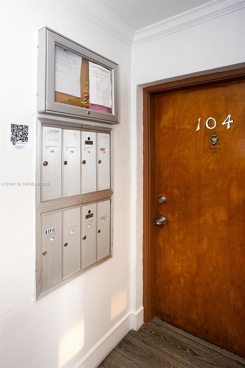 Wall-mounted metal mail collection system with integrated lockable notice board and wood-finish entry door featuring metallic hardware