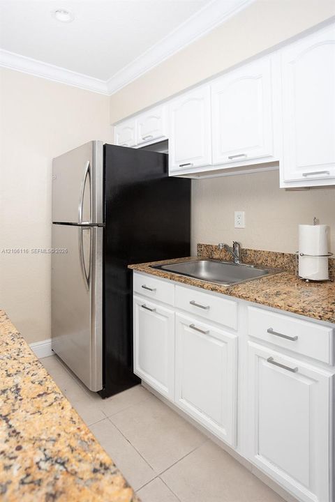 Kitchenette area featuring white shaker-style cabinetry, stone-surface countertops, stainless steel drop-in sink with faucet, and stainless steel refrigerator