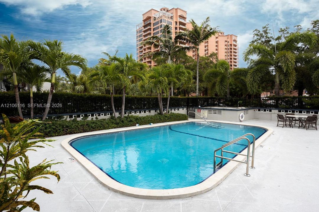 Outdoor swimming pool featuring a concrete deck, built-in metal handrails, integrated landscaping, and mature palm trees