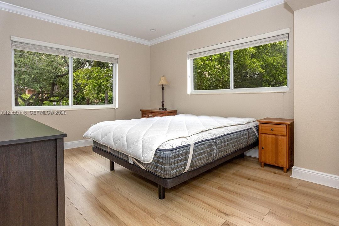 Neutral-toned walls featuring crown molding, wood-finish flooring, and dual picture windows with horizontal blinds