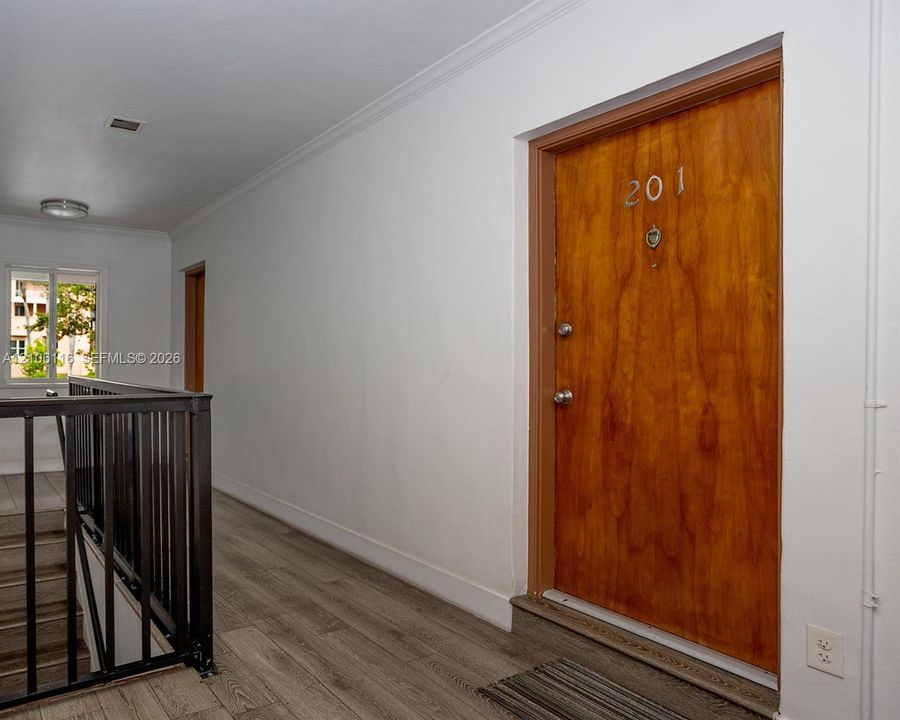 Solid wood-finish door with a metallic knocker, wood-finish flooring, and black metal railing