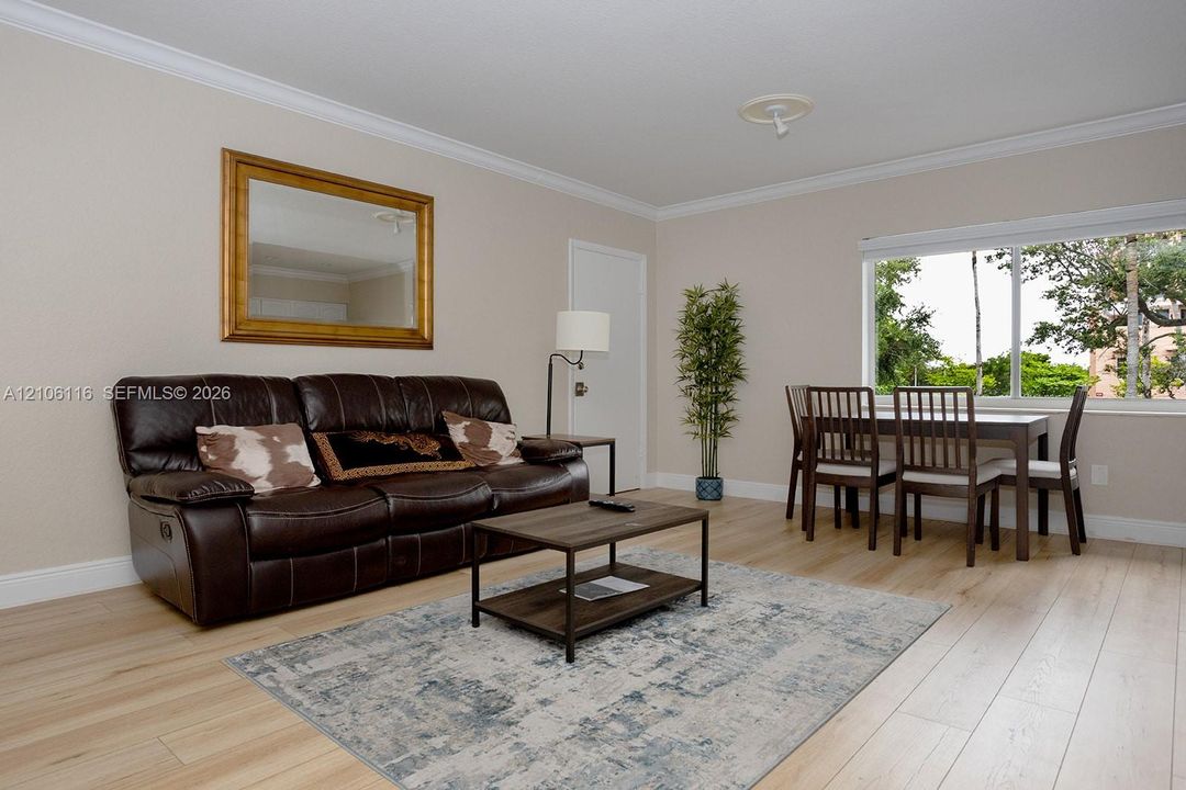 Living area featuring light-toned wood-finish flooring, crown molding, neutral wall finishes, and a wide horizontal window