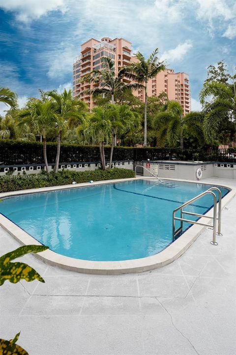 Swimming pool with metal handrails, concrete decking, mature palm trees, and perimeter landscaping
