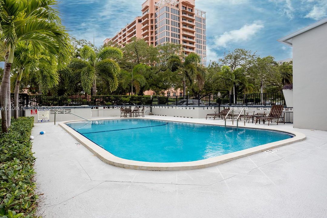 In-ground swimming pool featuring a concrete deck, metal handrail, perimeter fence, and mature palm landscaping
