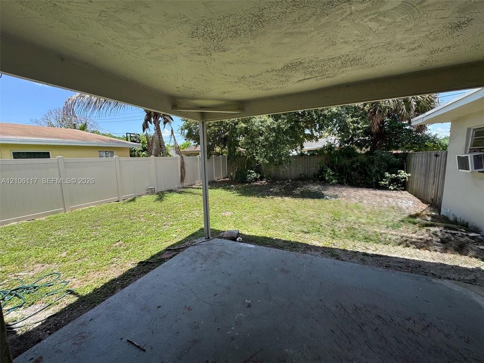 Covered concrete patio overlooking a private backyard enclosed by vinyl fencing with mature landscaping