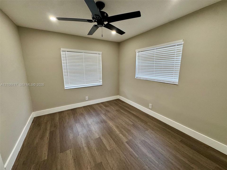 Neutral wall finishes, wood-finish flooring, two windows with horizontal blinds, and a ceiling fan with integrated lighting