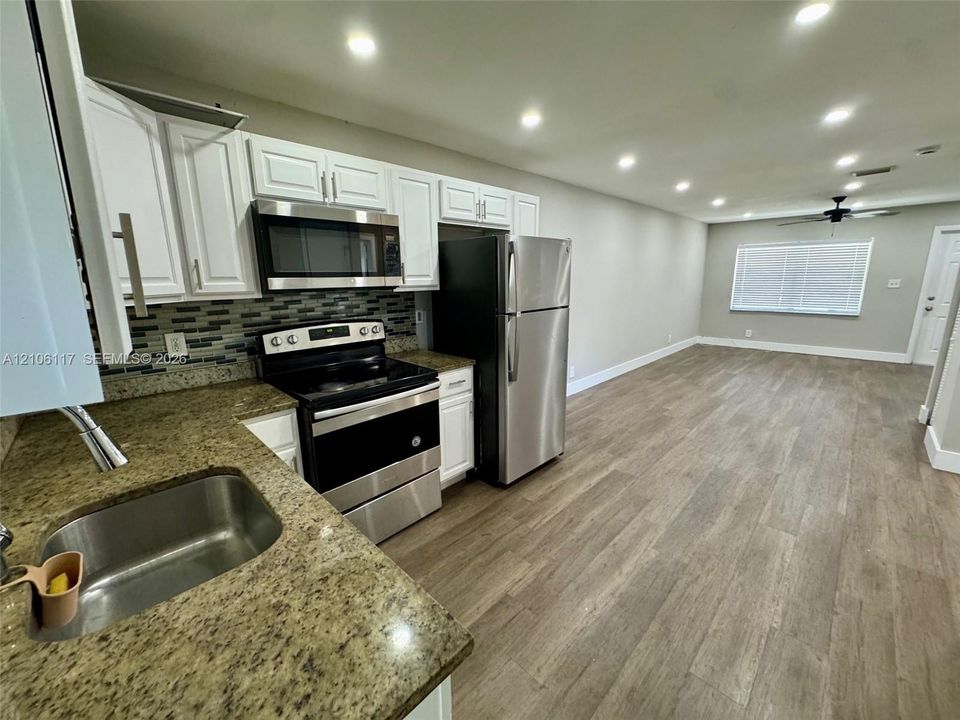 Kitchen featuring white shaker-style cabinetry, stone countertops, stainless steel appliances, a tile backsplash, and wood-finish flooring