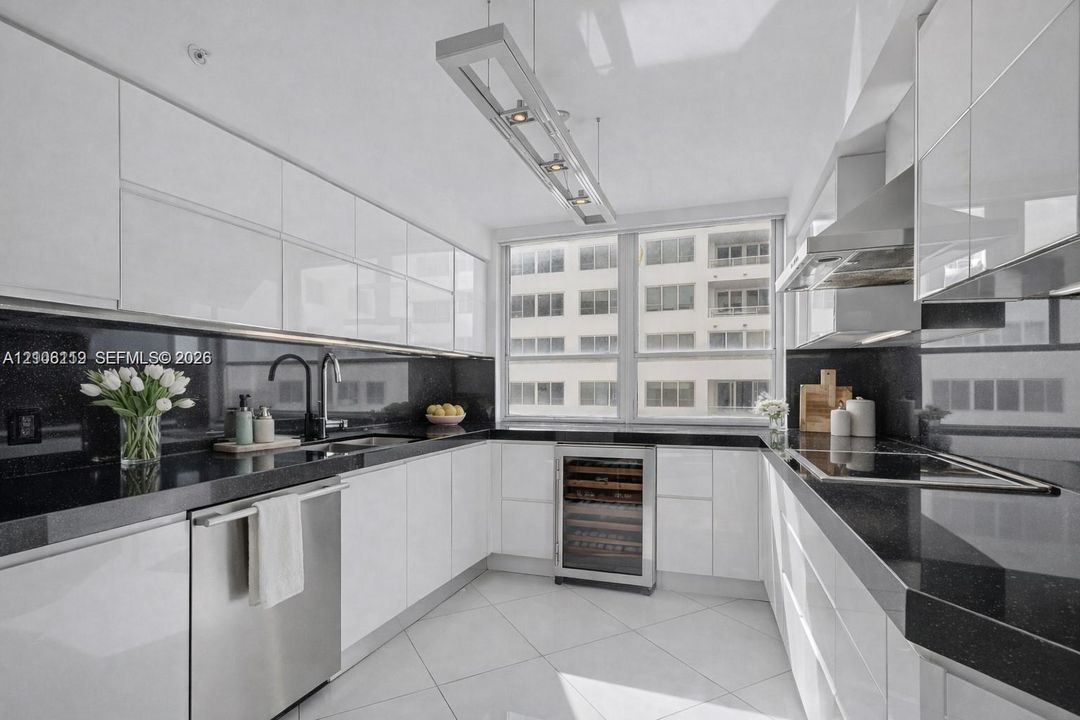 Kitchen featuring high-gloss white cabinetry, dark stone countertops, stainless steel appliances, a built-in wine cooler, and a linear pendant light fixture