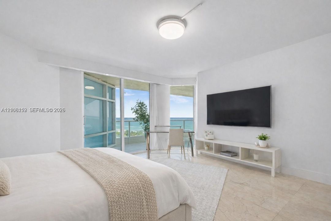 Floor-to-ceiling glass sliders, stone tile flooring, circular flush-mount ceiling light, and coastal ocean horizon