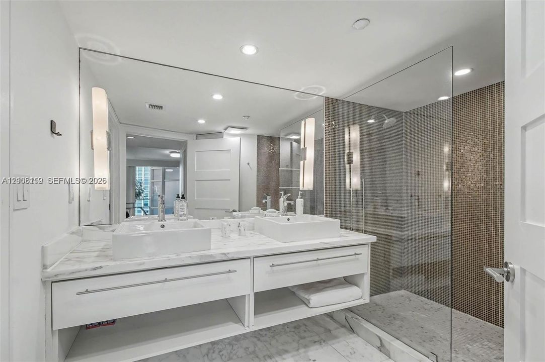 Floating vanity with dual rectangular vessel sinks, expansive wall-to-wall mirror, glass-enclosed shower with mosaic wall tiling, and stone flooring