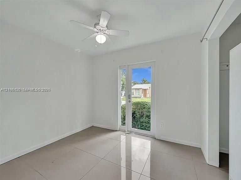 Neutral-toned large-format tile flooring, ceiling-mounted light fixture with fan, and a glass-paneled exterior door