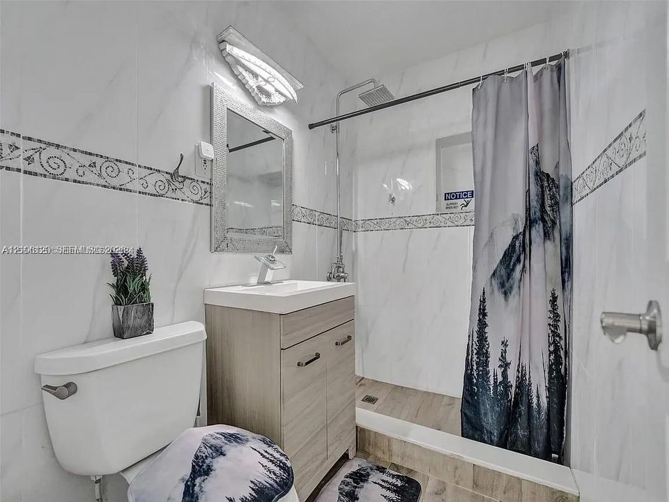 Full-height wall tiling featuring decorative accents, wood-finish vanity with a rectangular sink, wall-mounted mirror, and a ceiling-mounted rainfall showerhead