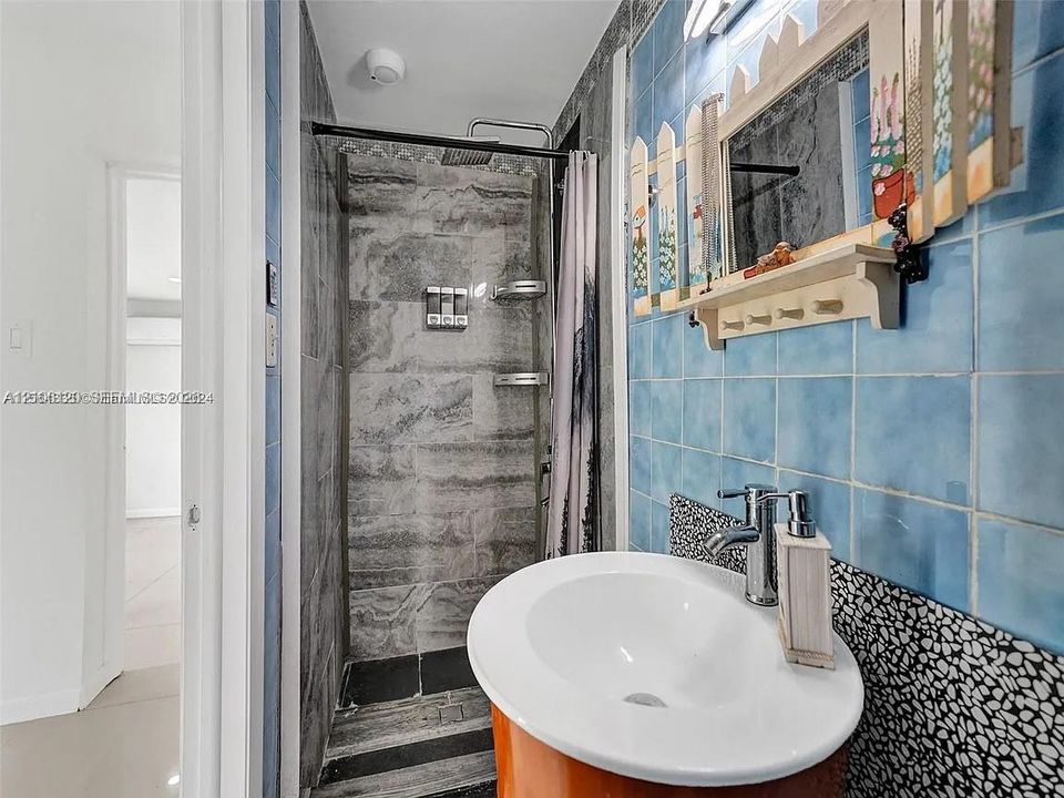 Bathroom featuring a shower stall with stone-finish wall tile, circular vanity with a white vessel sink, polished chrome faucet, and blue square wall tile accents