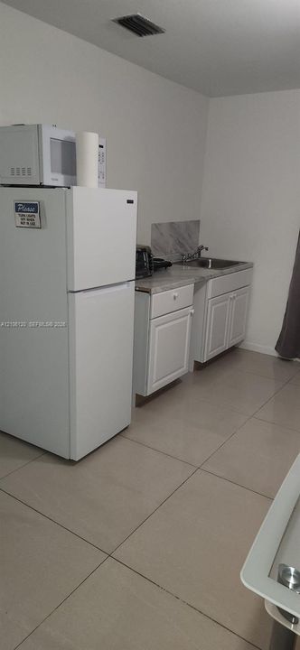 Kitchenette featuring white cabinetry, stone-finish countertops, stainless steel sink with faucet, and tile flooring