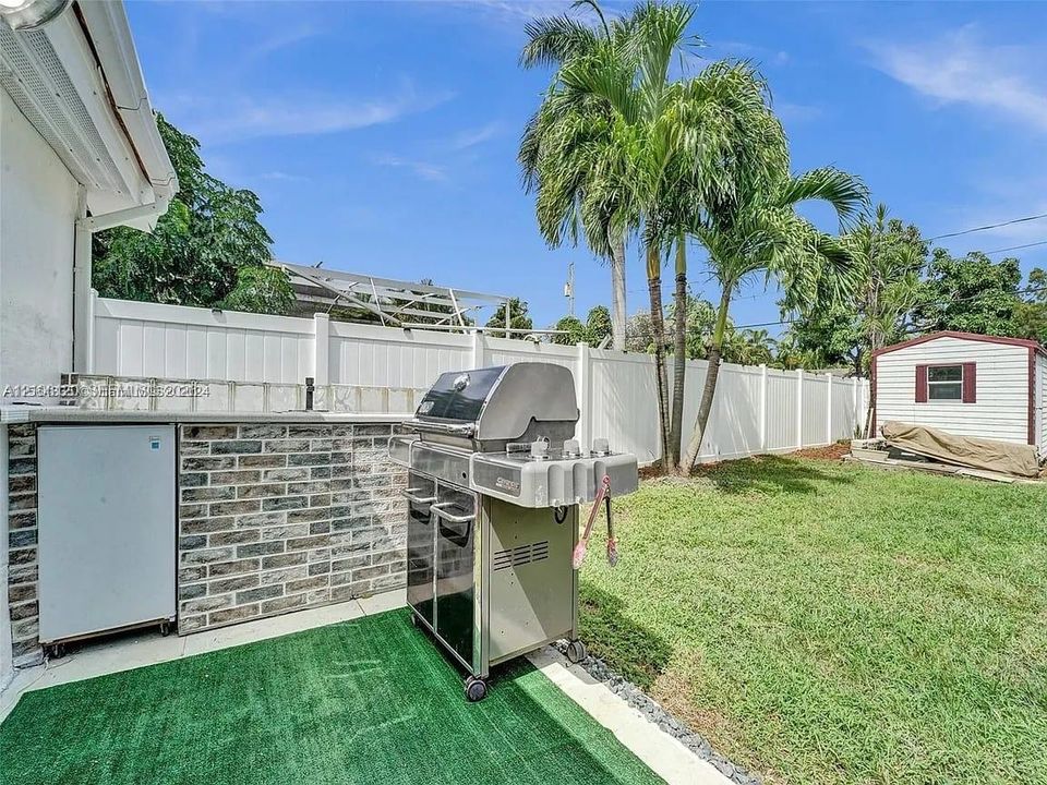 Outdoor grilling area featuring a brick base, integrated cabinetry, white vinyl privacy fencing, manicured lawn, and mature palm trees