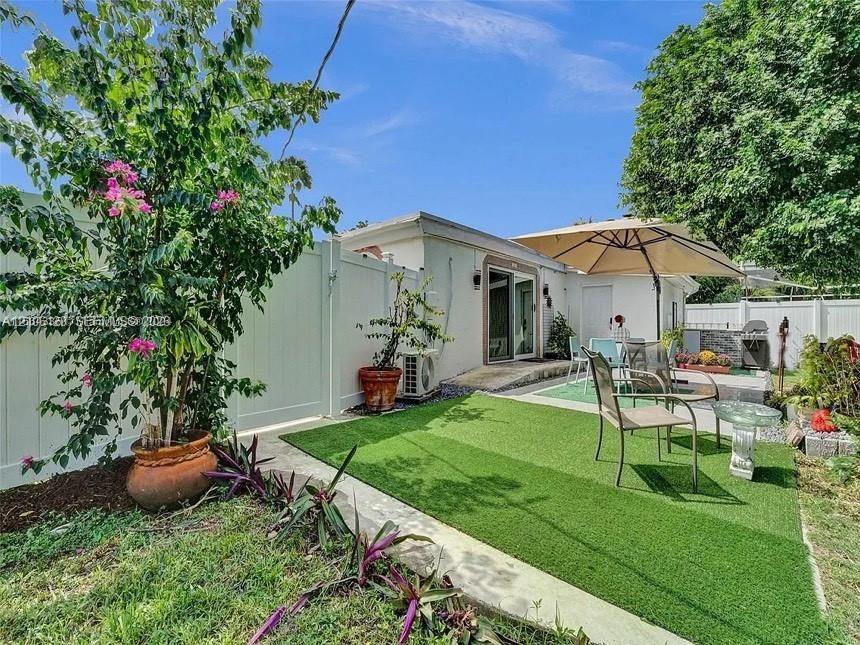 Private backyard featuring synthetic turf, white vinyl fencing, a concrete patio, and a masonry outdoor cooking station
