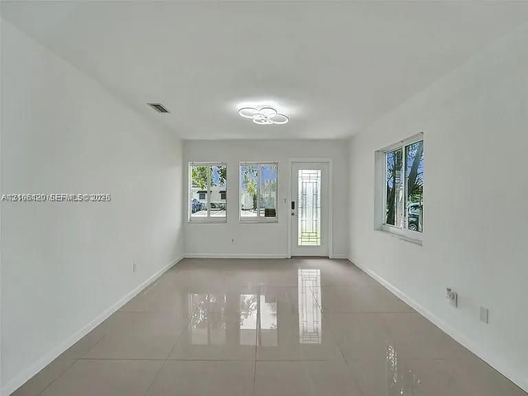 Interior space featuring large-format ceramic tile flooring, neutral walls, multi-pane windows, a decorative glass-panel exterior door, and modern multi-ring flush-mount lighting