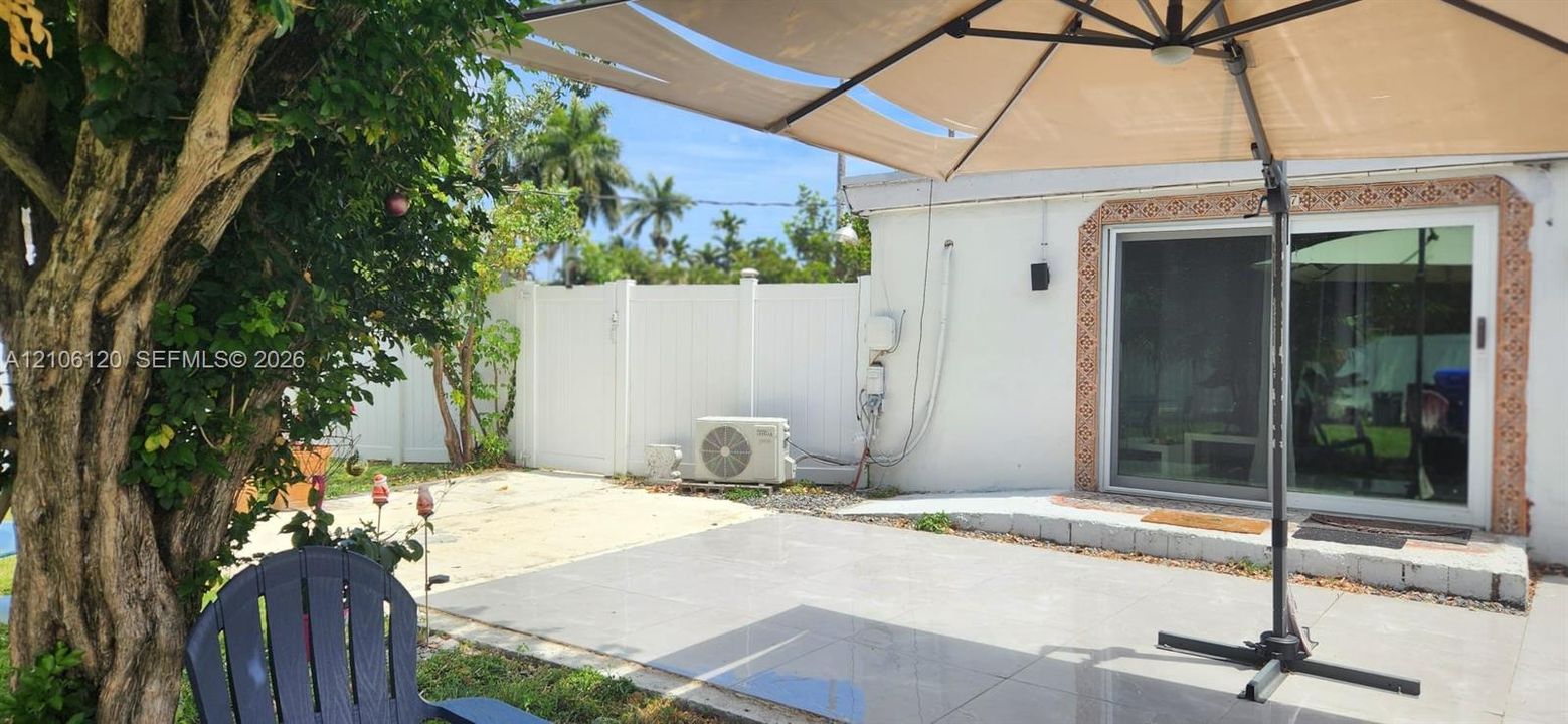 Outdoor patio area with large-format tile flooring, white vinyl privacy fencing, and sliding glass door access to the residence