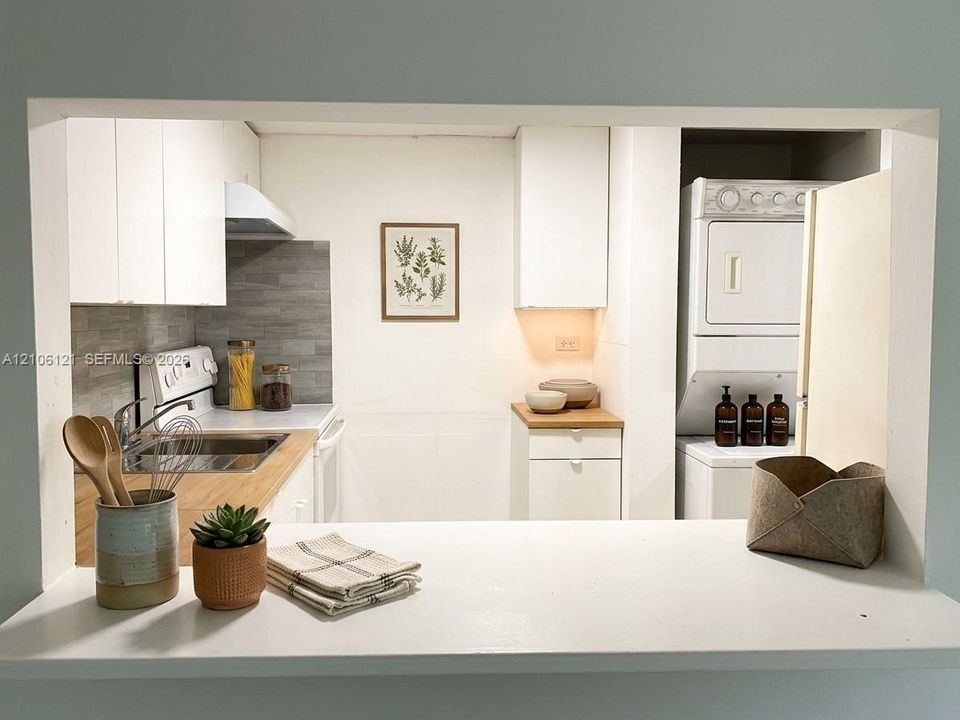 Kitchen featuring white cabinetry, wood-surface countertops, gray horizontal tile backsplash, and a stacked laundry unit