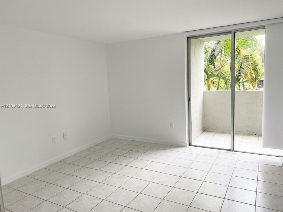 Neutral-toned tile flooring, white walls, and a sliding glass door providing access to a private balcony