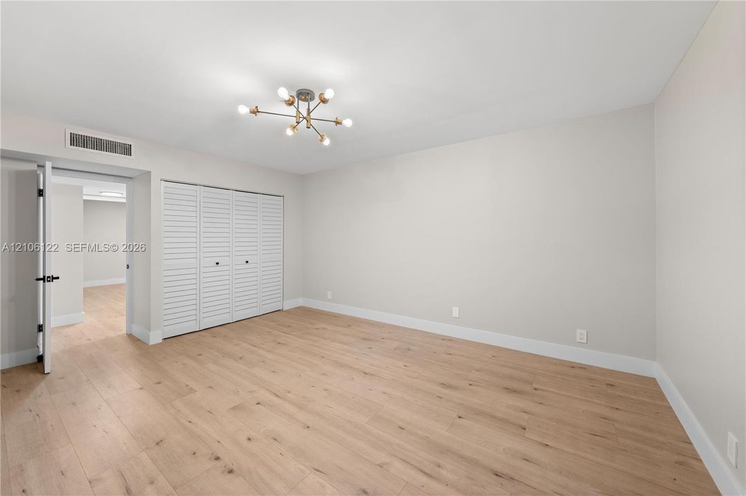 Room featuring wood-finish flooring, multi-light sputnik chandelier, and floor-to-ceiling louvered-door closet