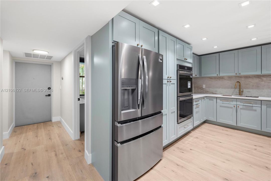 Kitchen featuring light blue shaker-style cabinetry, stainless steel French-door refrigerator, built-in double wall oven, stone-surface backsplash, and wood-finish flooring