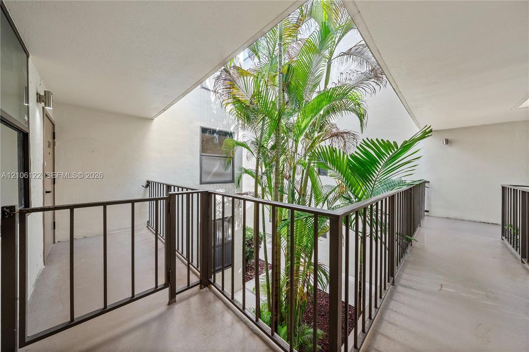 Open-air atrium featuring a central garden bed with mature palms and metal perimeter railings