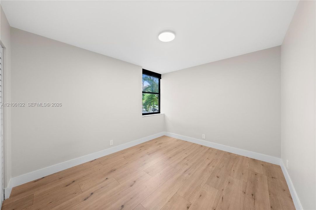 Neutral interior space featuring wood-finish flooring, crisp white wall paint, and a single window with a black frame