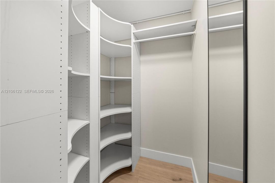 Custom walk-in storage featuring white built-in shelving, curved corner units, integrated hanging rods, and wood-finish flooring