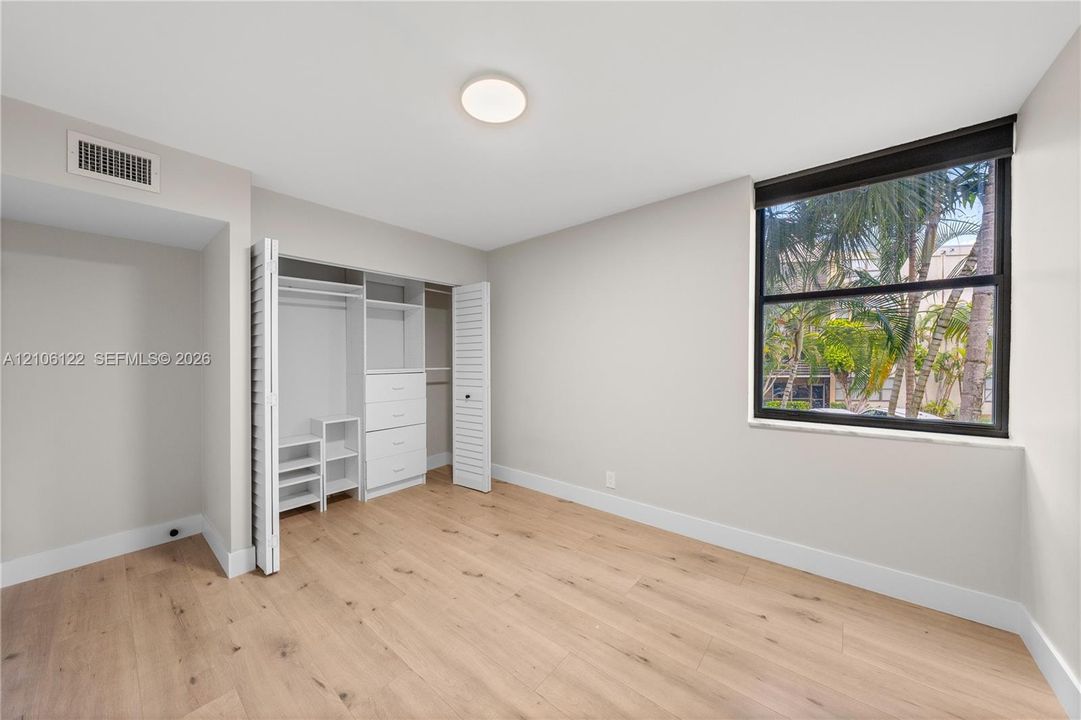 Room featuring wood-finish flooring, a large window with black framing, and a built-in closet system with integrated shelving and drawers