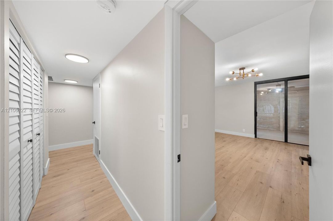 Wood-finish flooring, white louvered closet doors, flush-mount circular lighting, multi-bulb statement chandelier, and floor-to-ceiling glass sliding doors with black framing