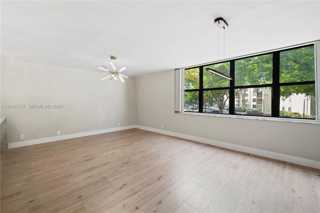 Expansive room featuring wood-finish flooring, large windows with black frames, a multi-arm sputnik chandelier, and a contemporary linear pendant light
