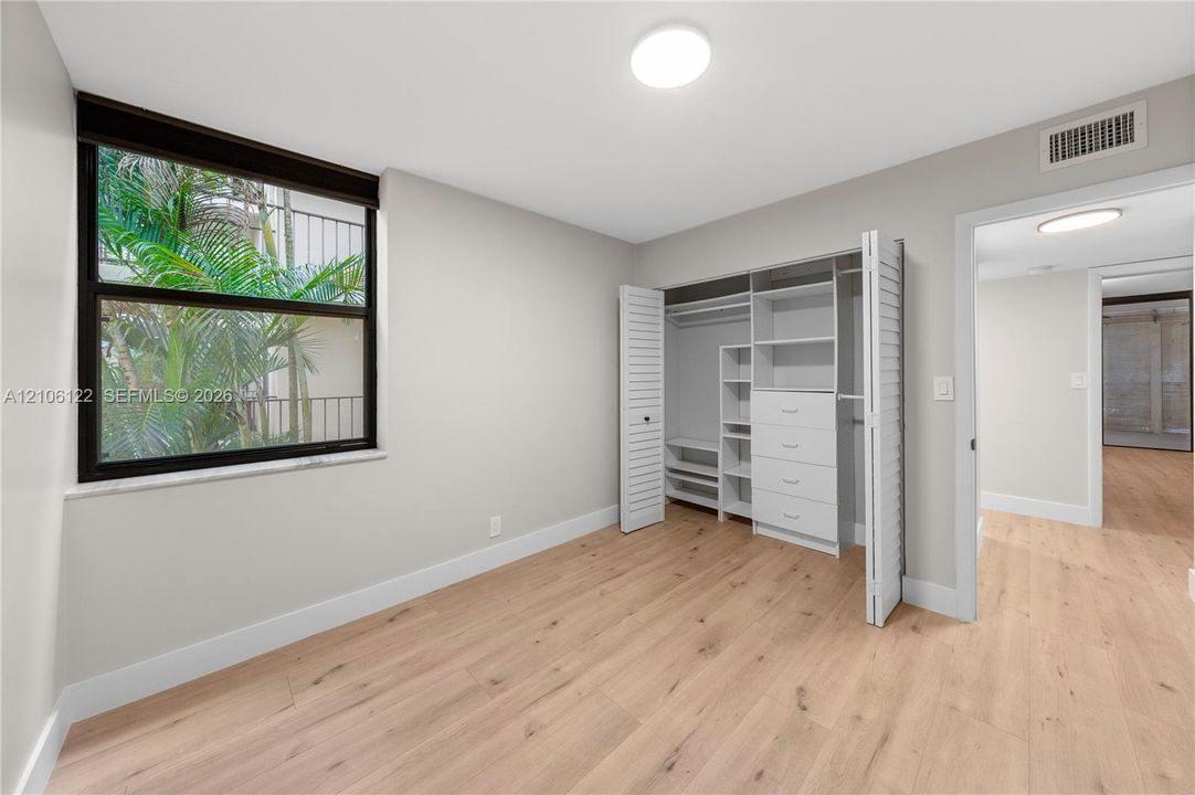 Neutral interior featuring wood-finish flooring, large window with dark frame, and built-in closet system with shelving and drawers