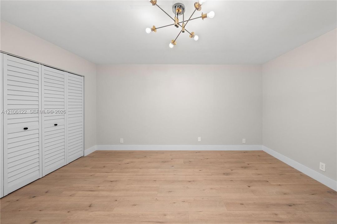 Wood-finish flooring, multi-panel louvered closet doors, and a modern multi-arm sputnik-style light fixture