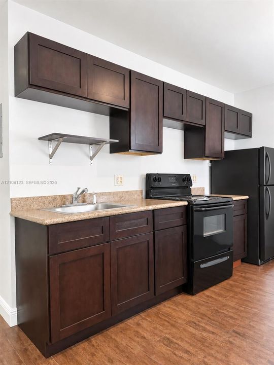 Dark wood cabinetry, stone-finish countertops, stainless steel sink, wall-mounted shelving, and wood-finish flooring
