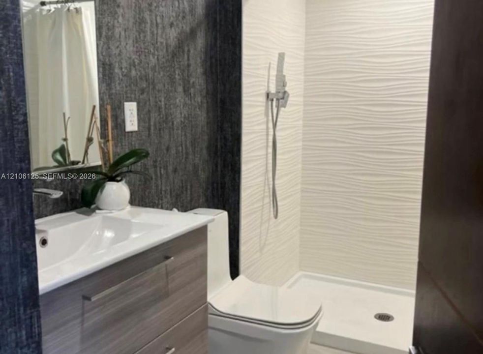 Bathroom featuring a floating vanity with a integrated sink, textured charcoal wall surfacing, a walk-in shower with white wavy-pattern tile, and a wall-mounted handheld shower fixture