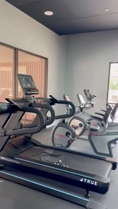 Fitness space featuring high ceilings, neutral wall tones, inset ceiling lighting, and large window panels