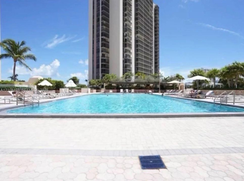 Large swimming pool with stone-paver decking, metal entry rails, and surrounding palm trees